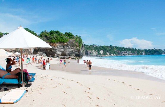 Tourists enjoy a bright sunny day at Dreamland Beach Bali with clear blue skies.