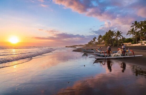 Two local Balinese fishermen preparing their traditional outrigger boat at Pasut Beach during sunset.