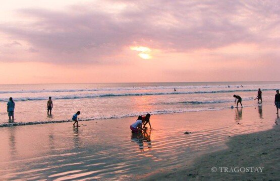 Children playing on the sand at Kuta Beach during a golden sunset in Bali.
