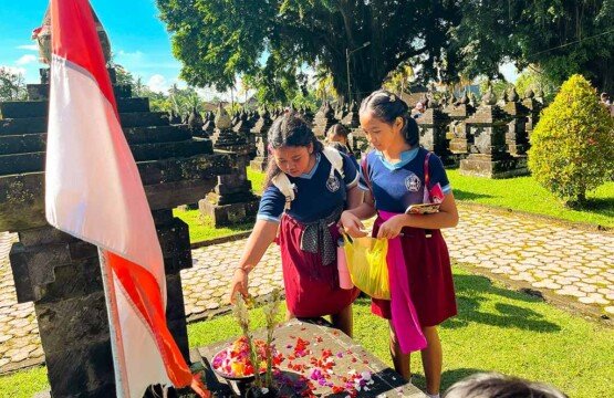 Two students scattering flower petals on heroes' graves at Puputan Margarana Monument.