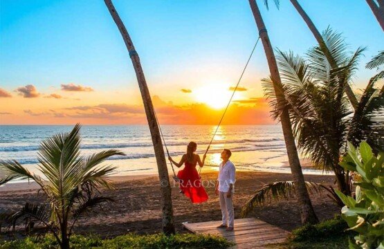 A tourist woman enjoying the iconic sunset swing at Pasut Beach with her partner watching from below.