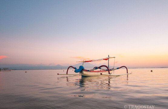 Sanur Beach sunrise with a traditional boat floating on the calm sea of Bali.