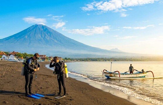 Two divers preparing their gear on Amed Beach with the majestic Mount Agung in the background.
