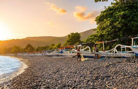 Local Balinese fishermen preparing traditional jukung boats during a warm sunrise at Amed Beach.