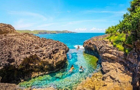 Three tourists swimming and having fun in the vibrant emerald pool of Angel's Billabong during a sunny day.