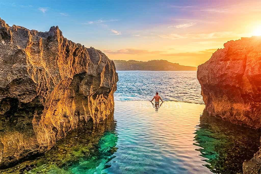 A man relaxing in the rock pool of Angel's Billabong while watching the sunset over the Indian Ocean.