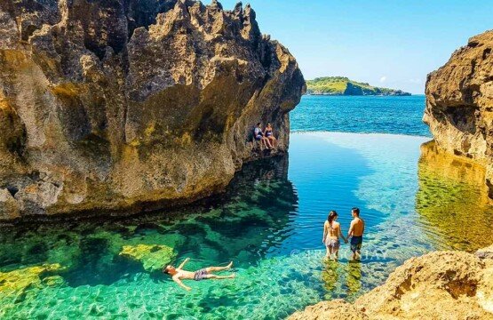 Several tourists enjoying the peaceful atmosphere and natural pool at Angel's Billabong during a clear morning.