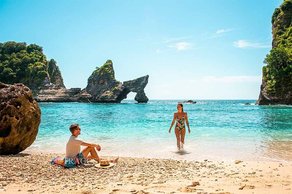 A tourist couple sitting on the sand and sunbathing under the bright midday sun at Atuh Beach.