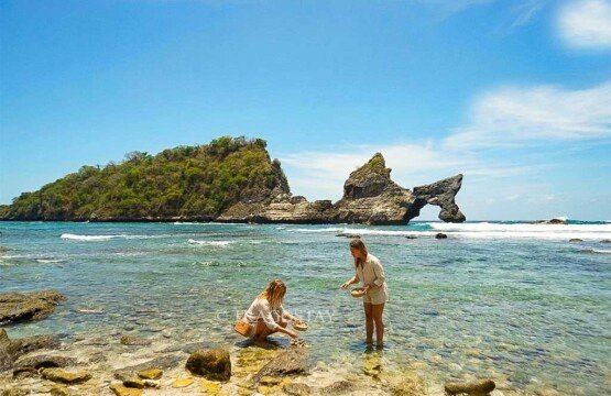 Two female tourists exploring the tide pools and searching for sea shells on Atuh Beach in the afternoon.