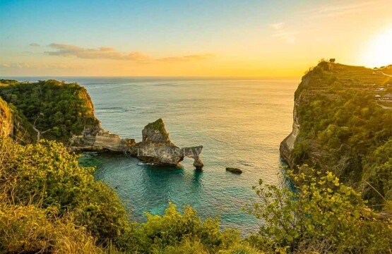 A breathtaking sunset view overlooking the bay and rock arches of Atuh Beach from a high hilltop.