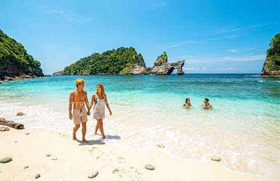 International tourists enjoying a swim and walking along the scenic white sand shore of Atuh Beach.