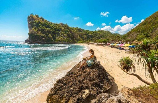 A female traveler sitting on a rock formation while gazing at the vast blue horizon at Atuh Beach.