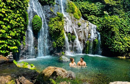 An international tourist couple happily wading and swimming together in the fresh waters of Banyumala Waterfall pool on a bright, sunny afternoon.