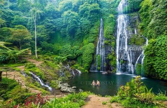 A high-angle view from the upper trails looking down at the wide emerald water basin and rocky shores of Banyumala Waterfall.