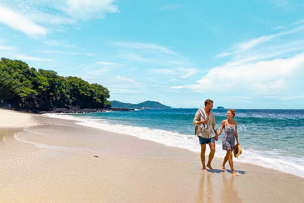 A tourist couple walking along the white sand shore of Bias Tugel Beach.