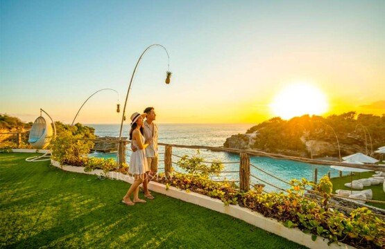 A romantic couple standing on a wooden deck watching a clear sunset over the Blue Lagoon horizon.