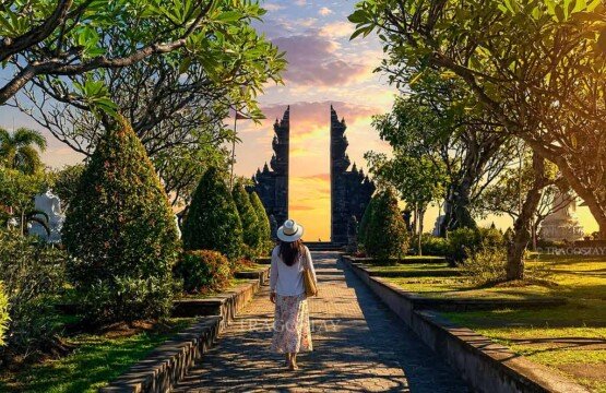 A female tourist walking along a stone pathway toward a grand Balinese-style Candi Bentar split gate inside Brahmavihara Arama.