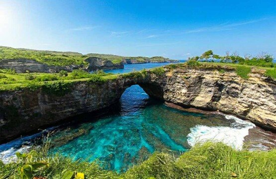 A wide-angle panoramic view of the rugged limestone cliffs and crashing waves at Broken Beach during the day.