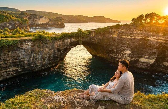 A romantic couple sitting on a cliffside ledge overlooking Broken Beach during the warm golden hour.