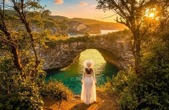 A woman standing peacefully while watching the sunset glow illuminate the natural stone bridge at Broken Beach.