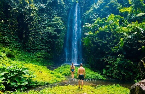 A couple of international tourists walking along a river path toward the hidden second cascade of Bunutin Waterfall.
