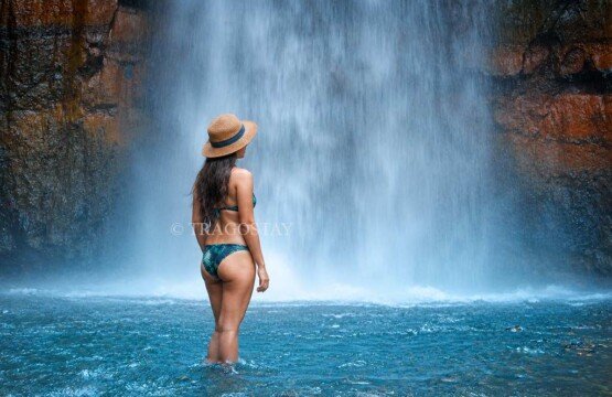 A young woman smiling and posing inside the clear, cool natural plunge pool at the base of Bunutin Waterfall.