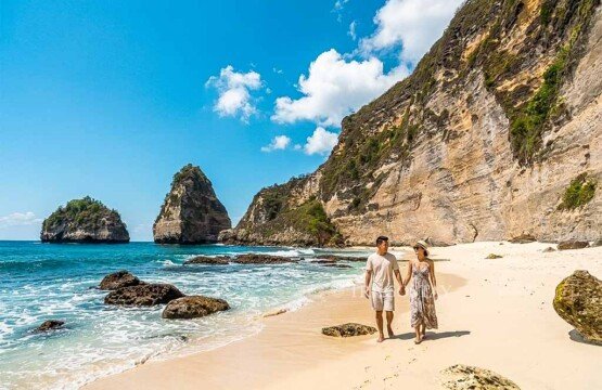 A tourist couple walking across the soft white sand of Diamond Beach during a bright sunny day.
