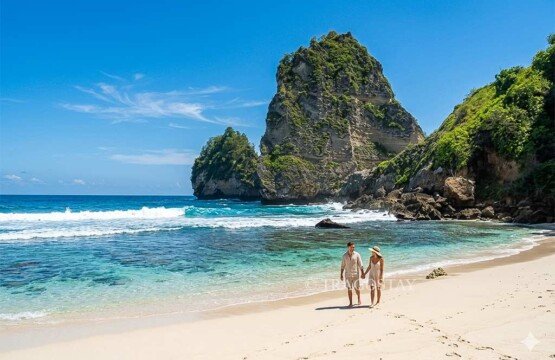 A romantic couple walking along the water's edge with the stunning backdrop of Diamond Beach.