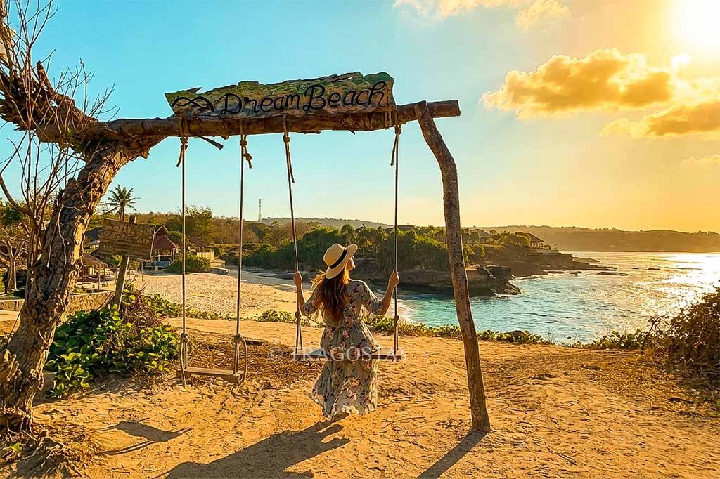 A female tourist having fun on a wooden swing at Dream Beach during a bright afternoon.