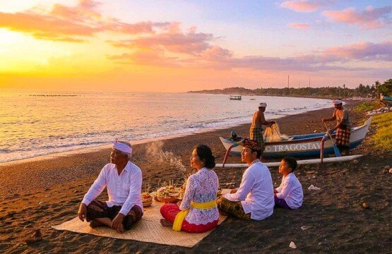 A vibrant sunset at Goa Lawah Beach showing Balinese Hindus sitting by the shore while fishermen prepare their boats.