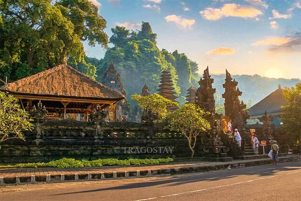 A scenic morning view of the front of Goa Lawah Temple as Balinese people in traditional dress enter the complex.