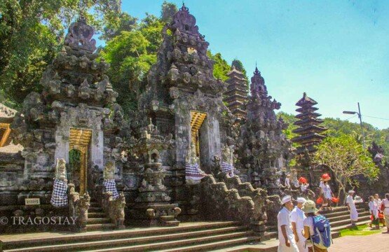 The ornate split gateway (Candi Bentar) of Goa Lawah Temple standing under a clear blue midday sky.