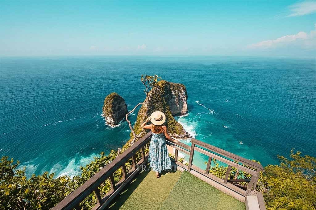 A female traveler standing at the edge of the Kelingking Beach lookout spot gazing at the vast ocean.