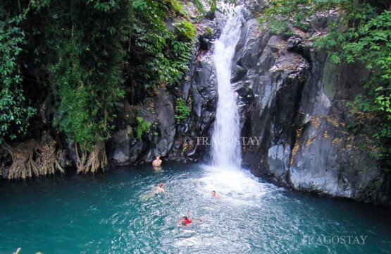 An adventurous tourist sliding down the smooth, wet rock face of Kroya cascade at Aling-aling Waterfall like a natural watersport ride.