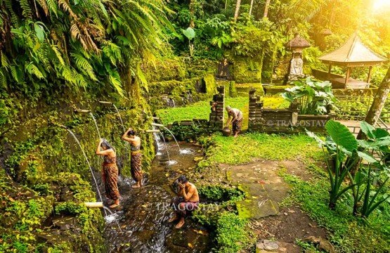 Several people bathing and cleansing themselves at the traditional stone water spouts in front of the Kuning Waterfall temple.