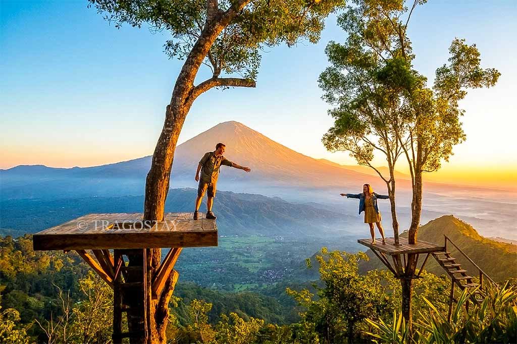 A romantic couple posing on elevated wooden platforms at Lahangan Sweet during a beautiful sunrise with Mount Agung in the background.
