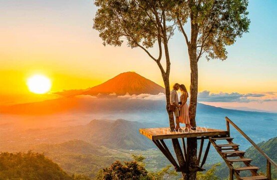 A romantic couple standing on a wooden platform at Lahangan Sweet with the golden sunset and Mount Agung as a backdrop.