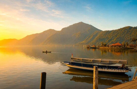 A local tour boat moored safely at a wooden lakeside dock on a clear and sunny morning at Lake Batur.