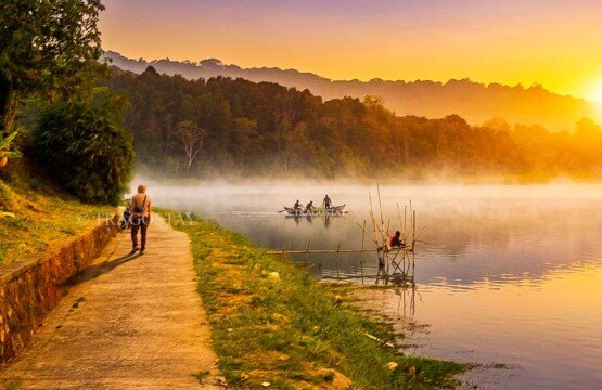A mesmerizing sunset casting rich orange and purple hues over the quiet waters and surrounding mountains of Lake Buyan.