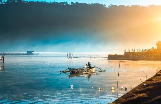 A traditional wooden fishing boat sailing smoothly across the calm waters of Lake Buyan during a golden morning sunrise.
