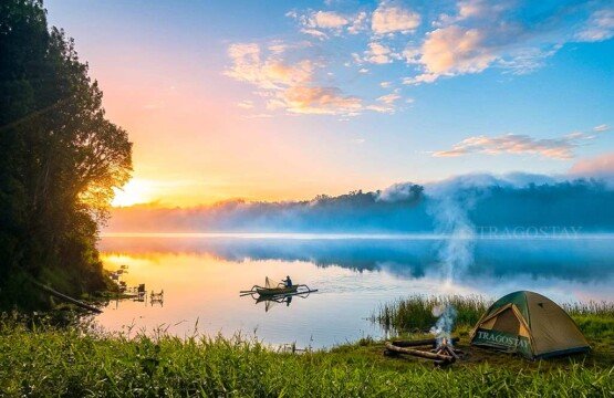 Colorful tents pitched at the green grassy camping ground area of Lake Tamblingan on a bright, clear morning.