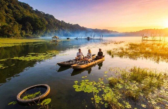 An adventurous tourist couple walking and exploring the scenic lakeside paths of Lake Tamblingan during a bright, sunny morning.