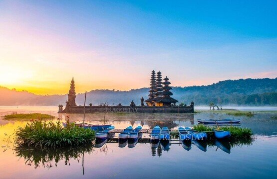 Several traditional Balinese wooden boats resting on the calm shores of Lake Tamblingan with an ancient Hindu temple in the background.