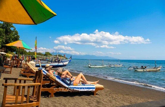 International tourists relaxing, walking, and enjoying their tropical vacation on the peaceful shores of Lovina Beach.