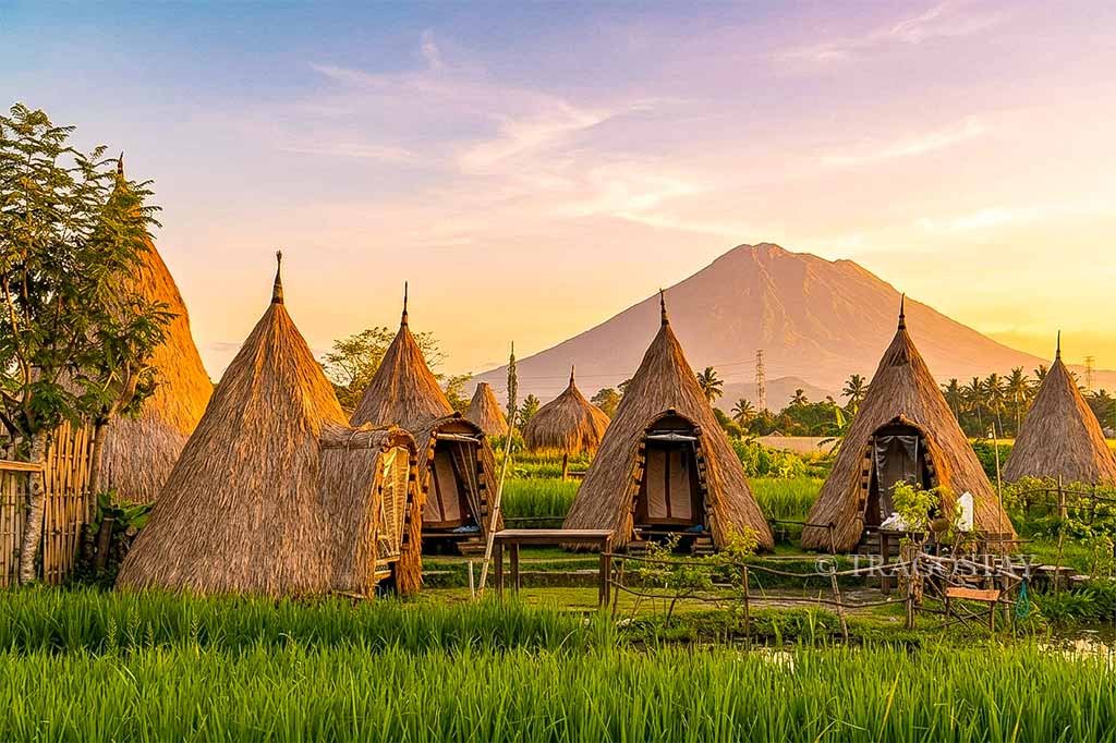Unique accommodation buildings at Maha Gangga Valley with a majestic Mount Agung backdrop during sunrise.