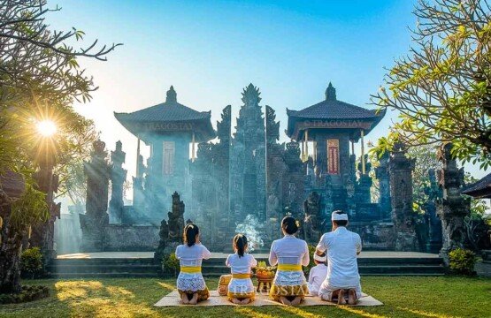 A Balinese Hindu family dressed in traditional ceremonial clothes kneeling down and praying in front of a shrine at Meduwe Karang Temple.