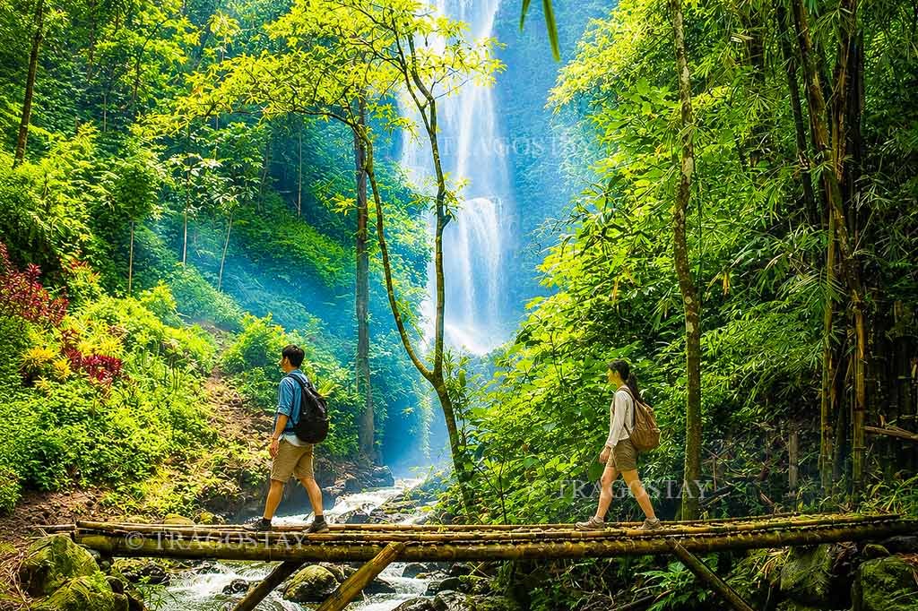 A rustic and iconic traditional bamboo footbridge crossing over a rushing river stream with lush green jungle plants around Melanting Waterfall.