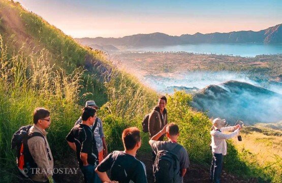 Several tourists walking down the slope of Mount Batur while admiring the picturesque green valley and lake below.
