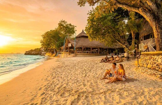 A group of tourists sitting on the soft white sand of Mushroom Bay enjoying the bright afternoon atmosphere.
