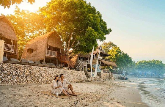 A tourist couple sitting on the white sand in front of a cozy beach hut at Mushroom Bay.